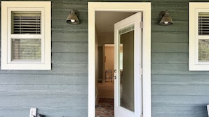 A hallway with a door leading to a room, a window with blinds, and a wall-mounted light fixture.