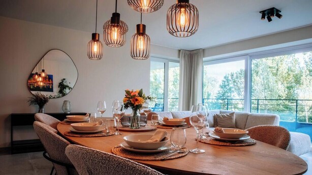 A dining area with a wooden table set for four, surrounded by cushioned chairs. - SAND–Modern apartment with garage near the beach (Ostend)