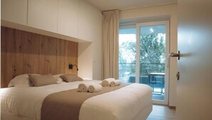 A bedroom with a wooden headboard, a bed with white linens, and a balcony with a table and chairs. - SAND–Modern apartment with garage near the beach (Ostend)