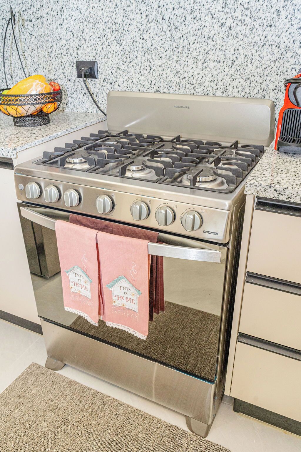 A kitchen with a stainless steel stove, oven, and a fruit basket on the countertop.