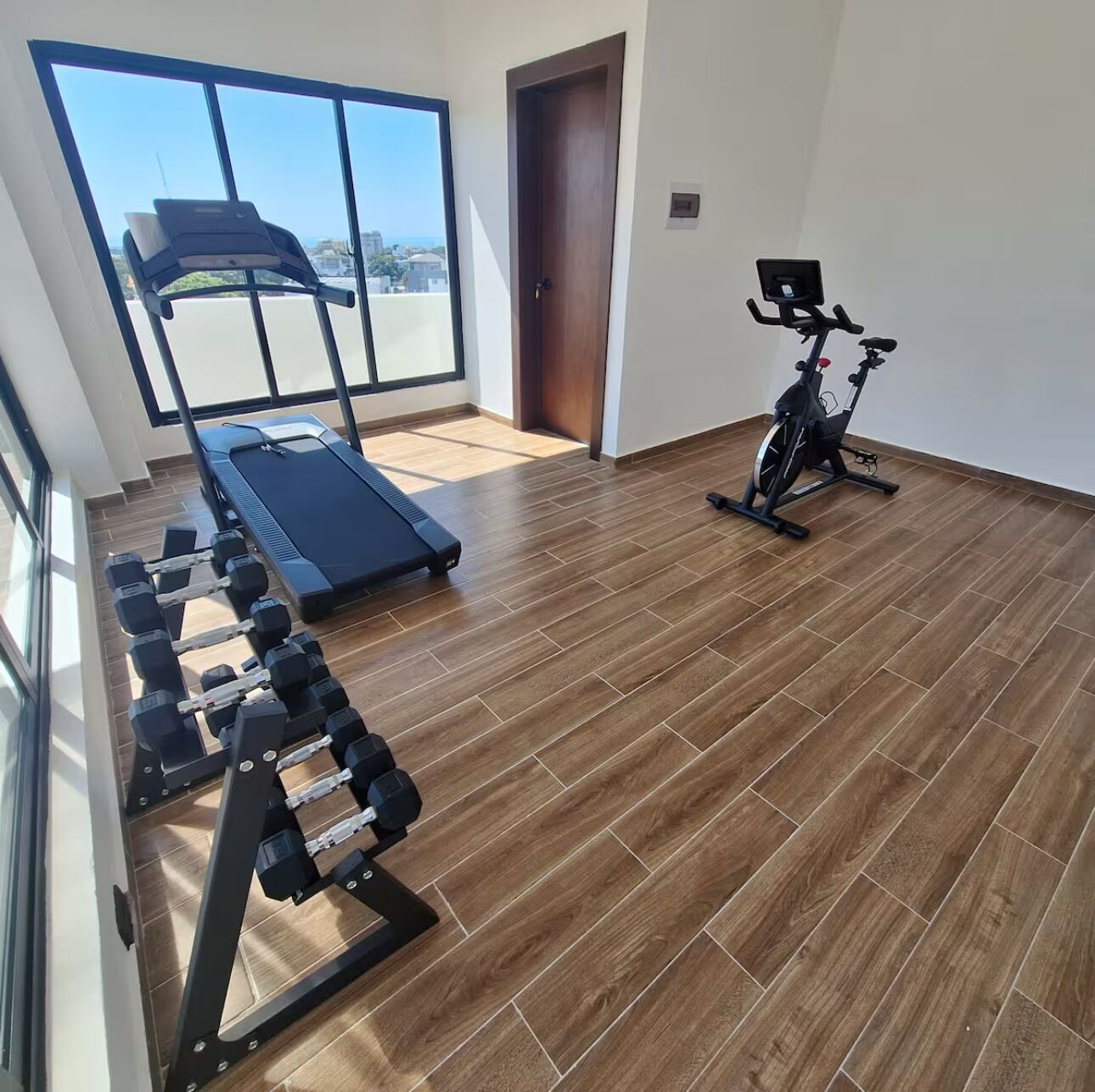 A spacious room with a treadmill, an exercise bike, and a dumbbell rack.