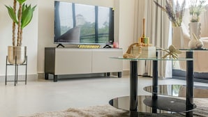 Una sala moderna con un televisor de pantalla plana, una mesa de centro de vidrio y una planta grande.