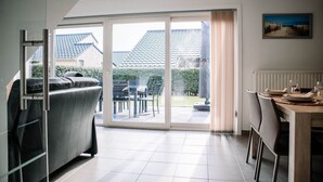 Eine moderne Küche mit Essbereich, eine Schiebetür zu einer Terrasse und Blick auf ein Haus mit einem Ziegeldach.