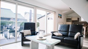 Ein modernes Wohnzimmer mit zwei schwarzen Ledersofas, einem Glastisch und großen Schiebeglasfenstern, die auf eine Außenpatio führen.