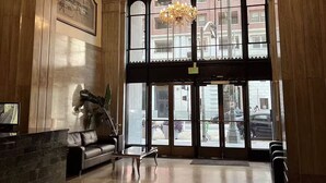 Eine geräumige Lobby mit einem beeindruckenden Kronleuchter, einem Empfangsbereich und großen Bogenfenstern mit Blick auf die Straße.