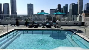 Ein Pool auf dem Dach mit Liegestühlen und Sonnenschirmen, umgeben von einer Stadtansicht.