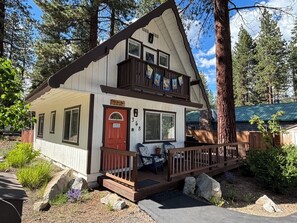 A two-story cabin with a balcony, a red door, and a deck with outdoor seating. - Charming North Lake Tahoe cabin near beaches and trails. (Tahoe Vista)