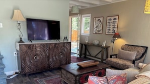 Un soggiorno con televisore, mobiletto in legno, divano a fantasia e tappeto.