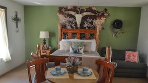 A room with a bed, a green wall, a wooden headboard, a sofa, a dining table with chairs, and a lamp.