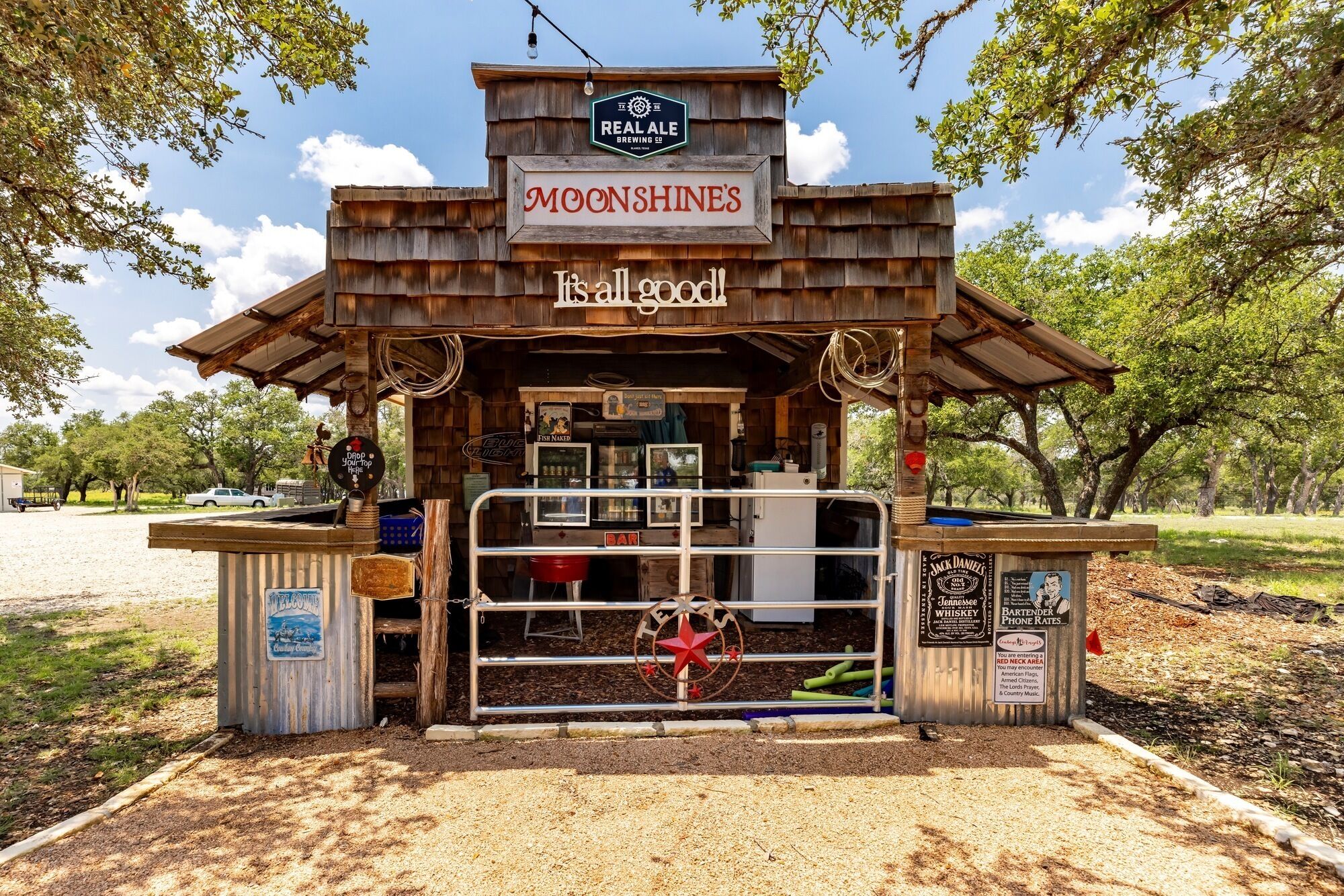 A rustic outdoor bar named 'MOONSHINE'S' with a wooden structure, a sign for 'REAL ALE BREWING CO', and a 'FISH NAKED' beer tap.