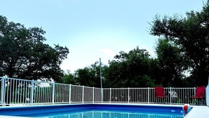 Una piscina con cerco blanco, rodeada de árboles y un cielo despejado.