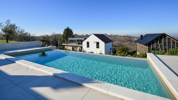 Un área de piscina moderna con agua azul cristalina, rodeada de arquitectura contemporánea y una vista panorámica.