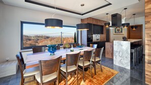 Un comedor moderno con un amplio ventanal, sillas de madera y una isla de mármol con taburetes.