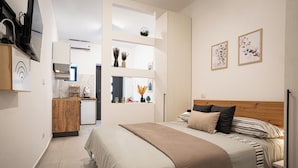 Ein modernes Hotelzimmer mit einem großen Bett, einem hölzernen Kopfteil, einer Küchenzeile mit Mikrowelle und Kaffeemaschine sowie Bildern an den Wänden.
