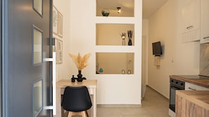A modern kitchen with a wooden countertop, a black chair, and a white wall with shelves. - 🎯 Piccolina - Studio Apartment in the Heart of Milazzo – Everything Within Easy Reach (Milazzo)