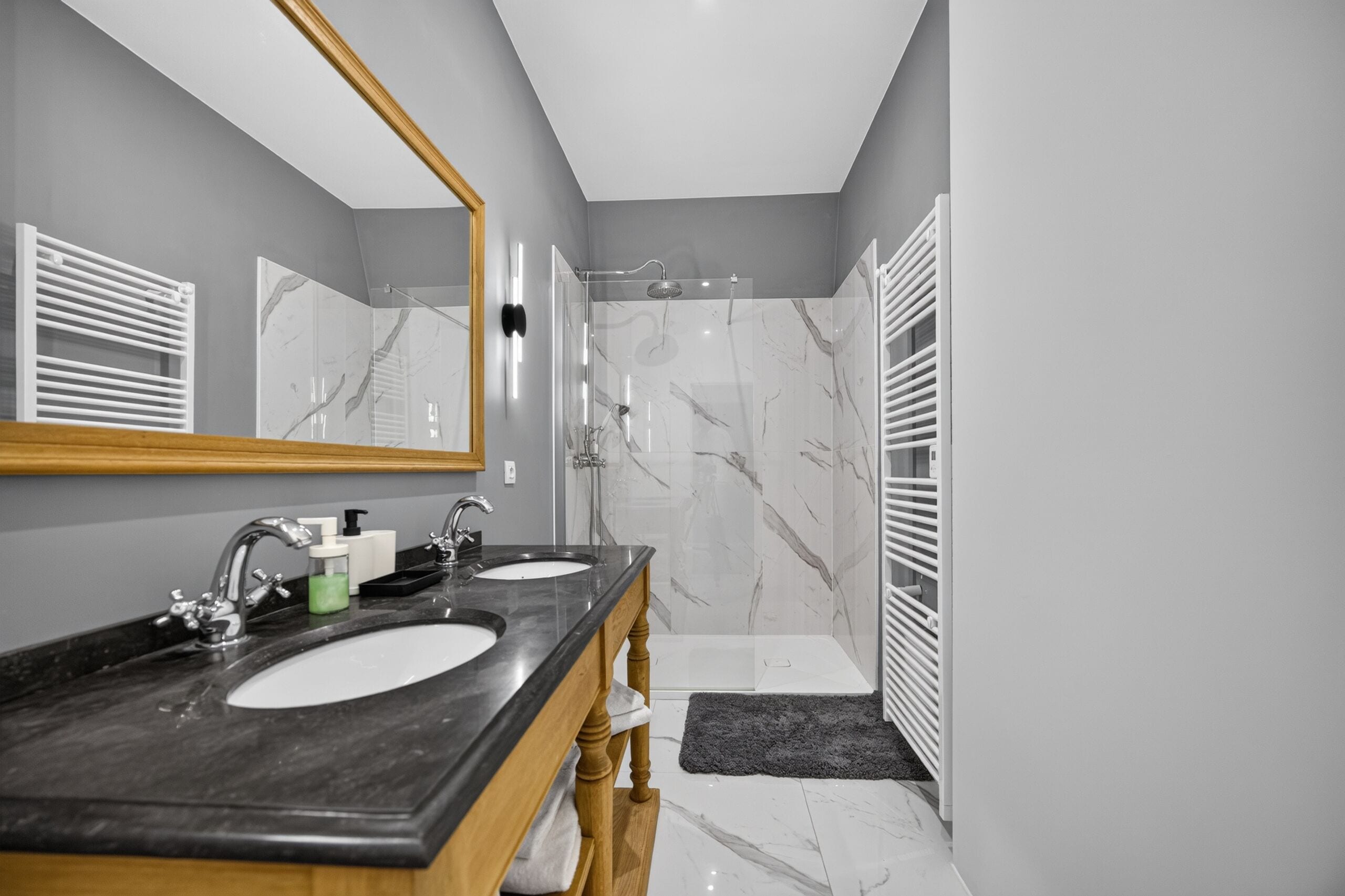 A modern bathroom with two sinks, a shower, and a large mirror.