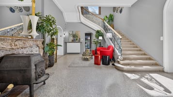 A spacious foyer with a grand staircase, a seating area with red chairs, and a variety of decorative plants.