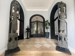 A hallway with a checkered floor, a black door, and two large sculptures on pedestals. - Villa Damseaux (Spa)