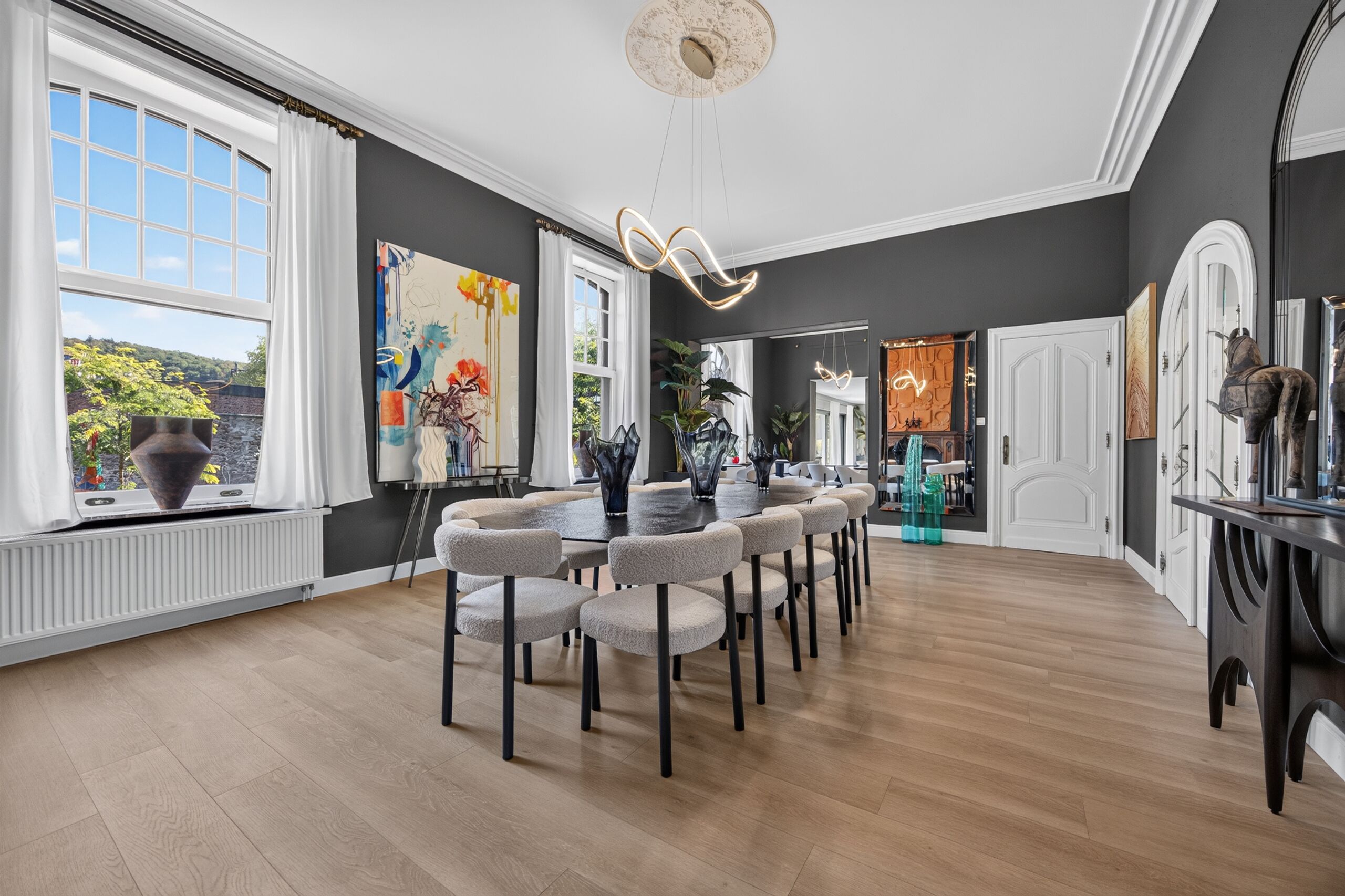 Een ruime eetruimte met een moderne kroonluchter, een groot raam met uitzicht en een eettafel met stoelen.
