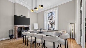 A conference room with a large table and chairs, a fireplace, a television, and a view of a building through a window. - Villa Damseaux (Spa)