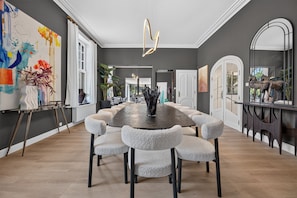 A spacious dining area with a long table and multiple chairs, a modern chandelier, and a large mirror. - Villa Damseaux (Spa)