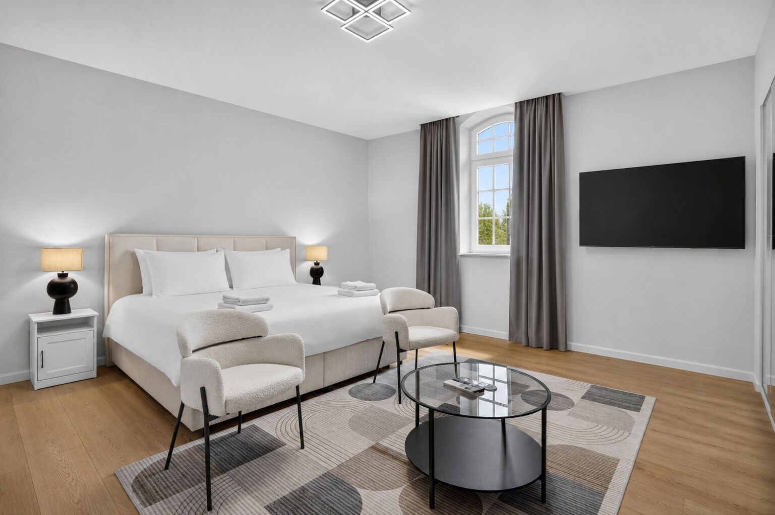 Une chambre d’hôtel moderne équipée d’un lit, de deux tables de chevet, d’un téléviseur, d’une table basse en verre et offrant une vue sur l’extérieur.