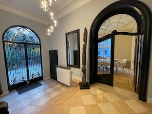 A modern interior with a checkered floor, a large arched doorway, a statue, and a dining area visible through the doorway. - Villa Damseaux (Spa)