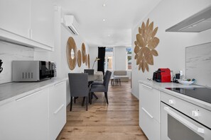 A modern kitchen with white cabinets, a microwave, a red coffee machine, and a dining area with a table and chairs. - Villa Damseaux (Spa)