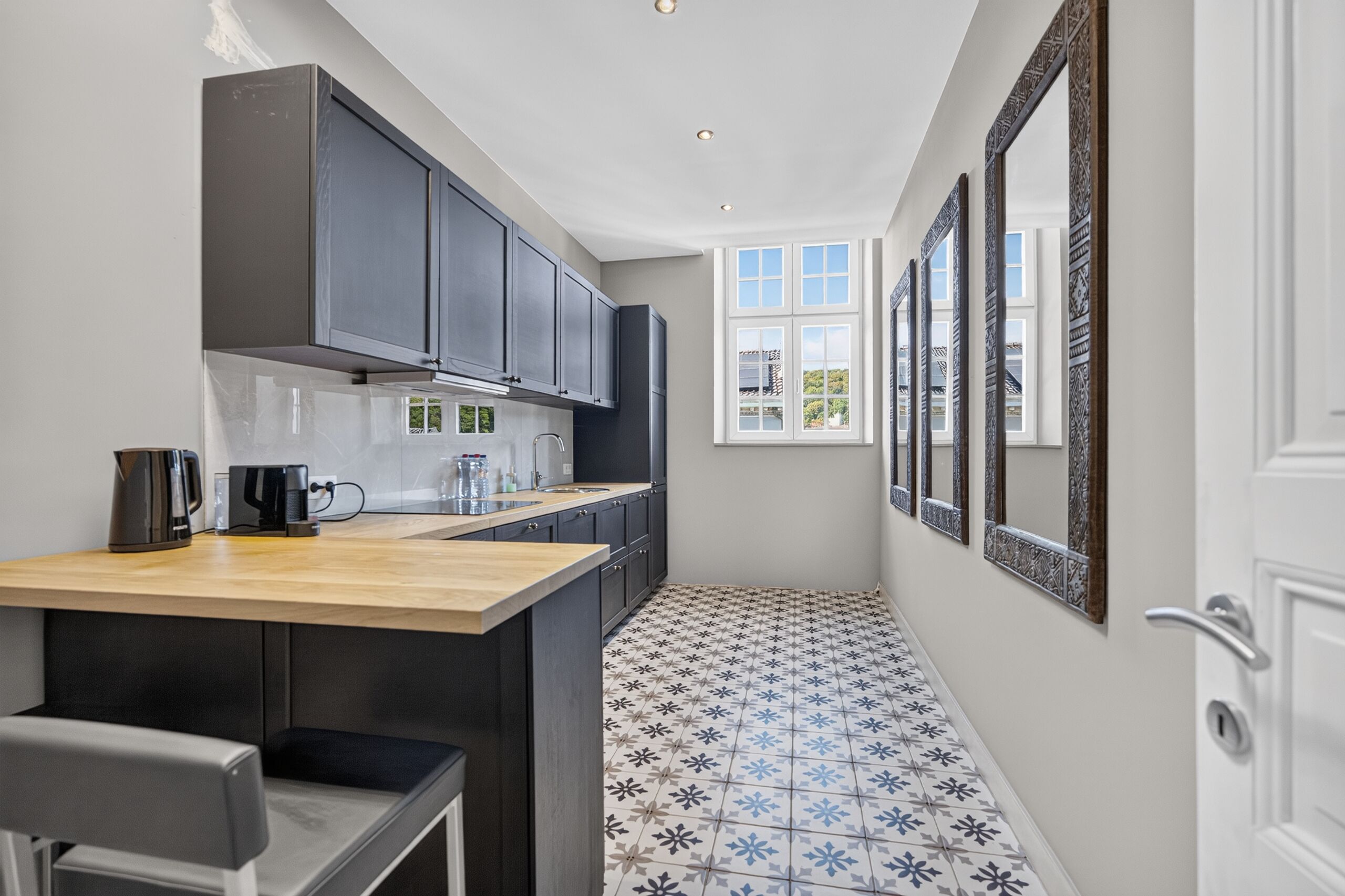 A narrow kitchen with dark cabinets, a wooden countertop, and a tiled floor.