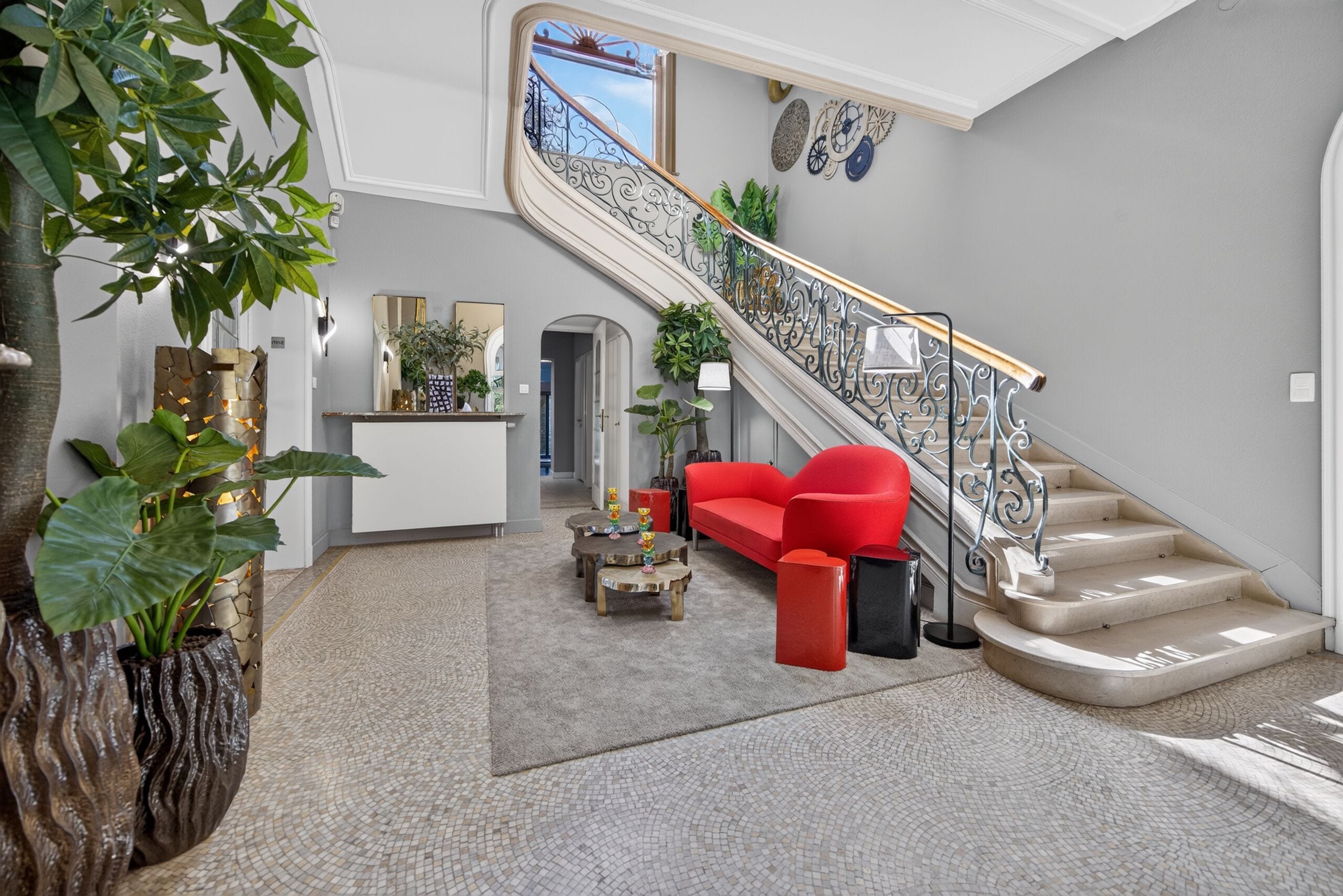 A spacious living area with a red sofa, a staircase with ornate railings, and a large potted plant.
