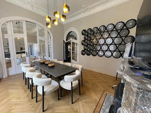 A dining area with a long table, six chairs, a chandelier, and a wall of decorative plates. - Villa Damseaux (Spa)