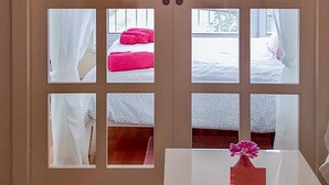 Una habitación de hotel con un ventanal grande, una cama con cabecera rosa y un jarrón con una flor rosa sobre una mesa.