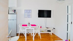 Un espacio habitable compacto con kitchenette, comedor y televisor montado en la pared.