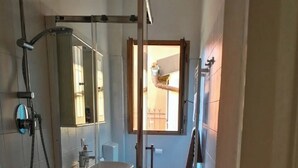 Een smalle badkamer met een douchecabine van glas, een wastafel en een toilet.