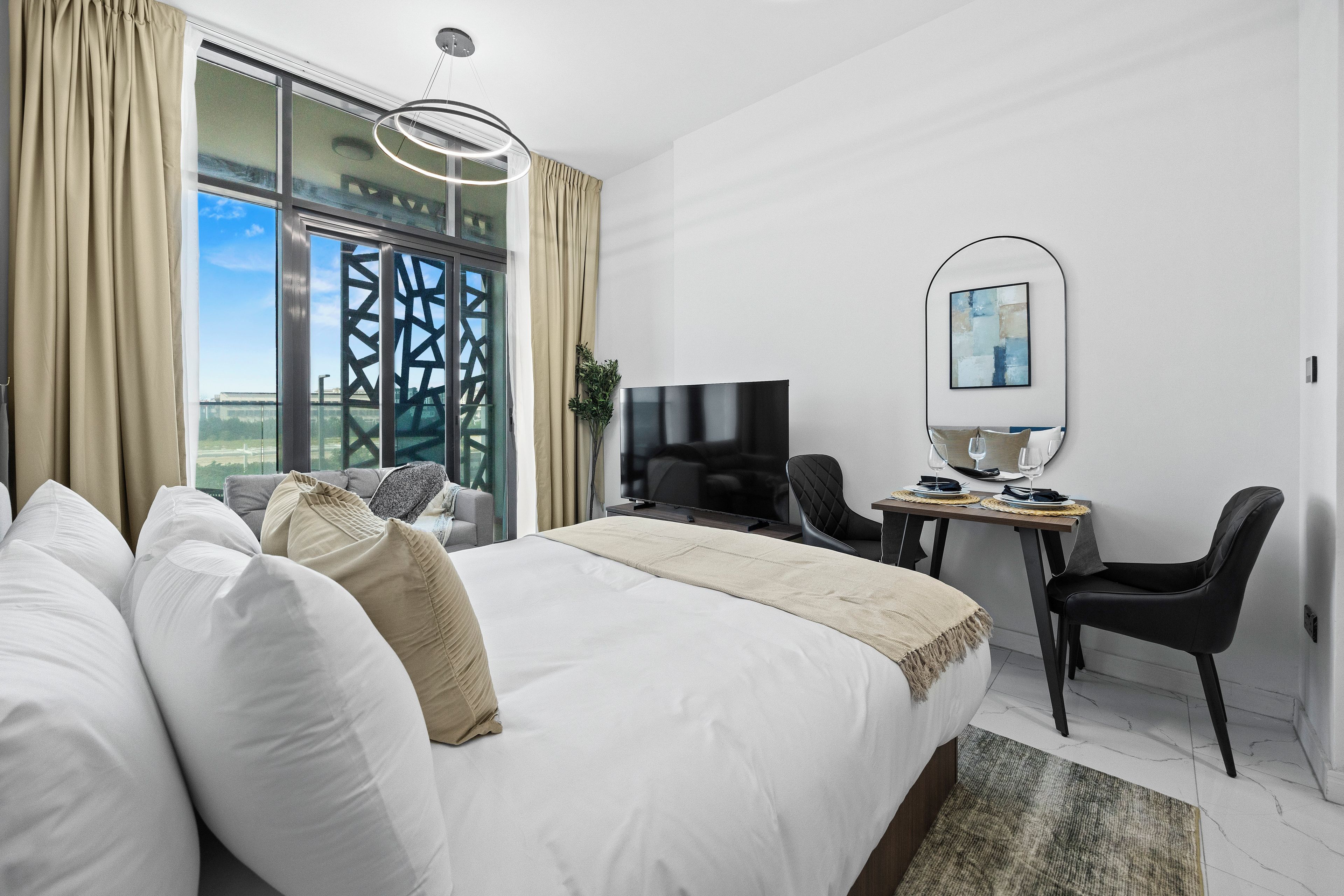 Una habitación de hotel moderna con una cama grande, un escritorio con televisor de pantalla plana y un área de comedor con sillas y una mesa.