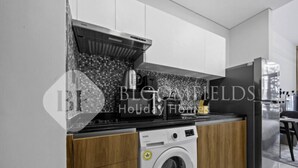 A modern kitchen with a washing machine, wooden cabinets, and a stainless steel refrigerator. - 106 Bloomfields Executive STU Gate Masdr (Madinat Zayed)