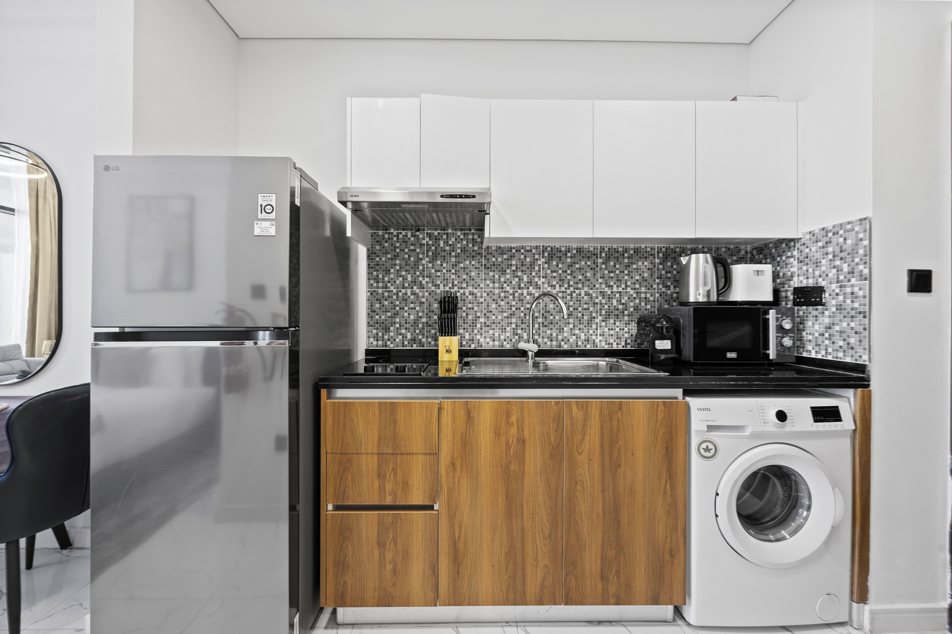 A compact kitchen with a stainless steel refrigerator, a washing machine, and a microwave.