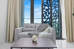 A modern living room with a grey sofa, a wooden coffee table, and a view of the sea through a window with a geometric pattern. - 106 Bloomfields Executive STU Gate Masdr (Madinat Zayed)