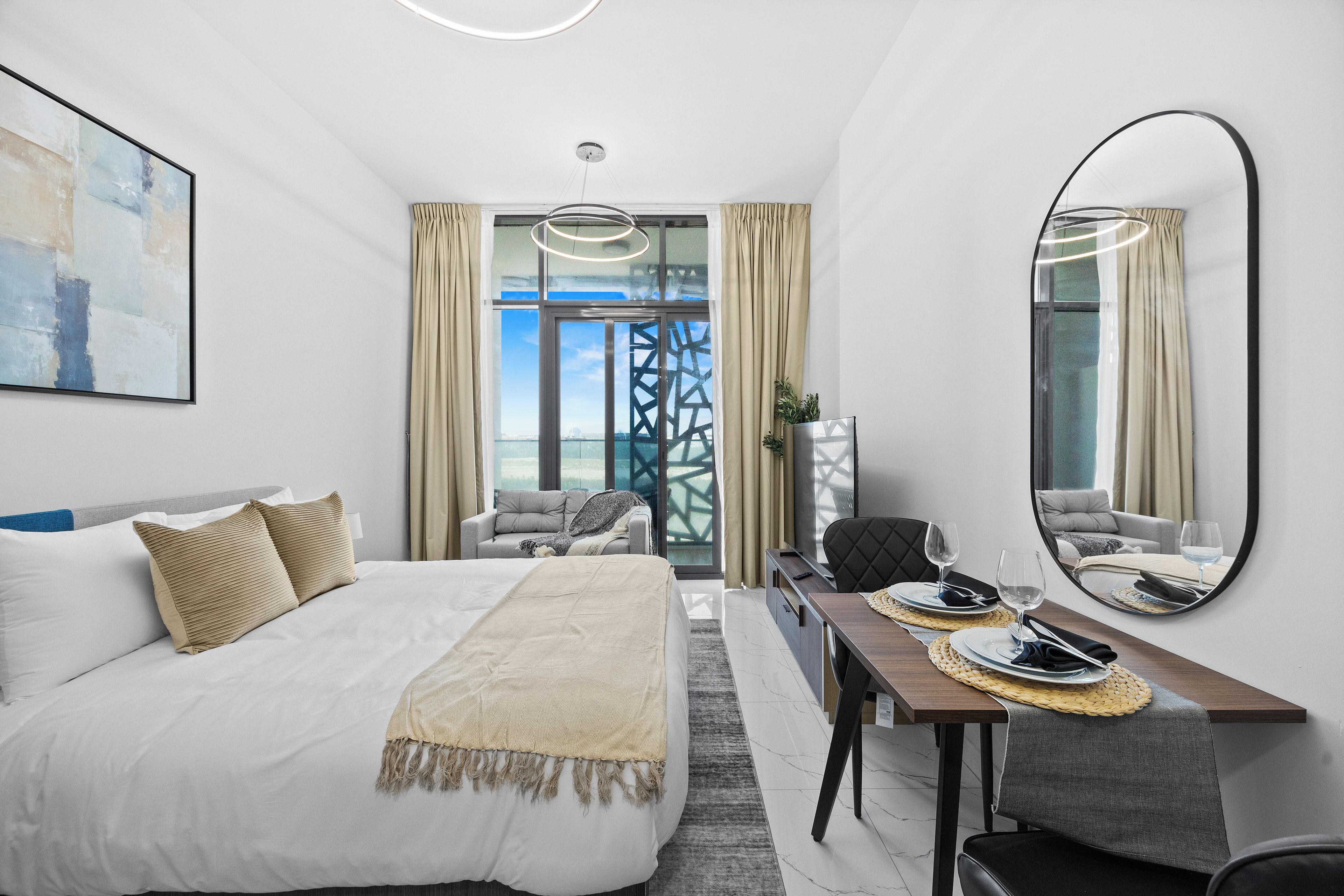 A hotel room with a bed, a dining table with chairs, a large mirror, and a view through a window.