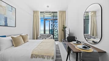 A hotel room with a bed, a dining table with chairs, a large mirror, and a view through a window.