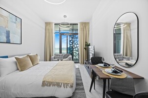 Una habitación de hotel con cama, una mesa de comedor con sillas, un espejo grande y vistas a través de una ventana.