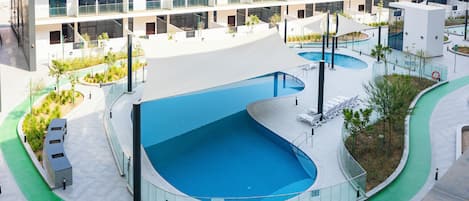A modern building with a swimming pool, outdoor seating, and a landscaped area.