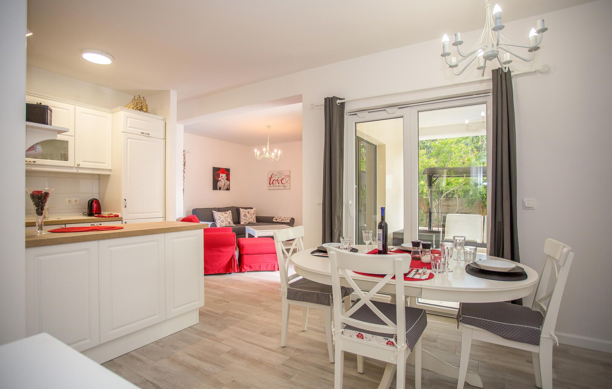 A modern kitchen with white cabinetry, a dining area with a round table and chairs, and a view through a large window.