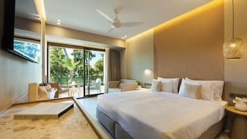 A modern hotel room with a large bed, a ceiling fan, a balcony with outdoor seating, and a view of greenery.