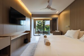 Une chambre d’hôtel moderne dotée d’une télévision à écran plat, d’un ventilateur de plafond, d’un grand lit avec du linge de lit blanc, d’un petit coin salon et offrant une vue sur l’extérieur grâce à une porte vitrée.