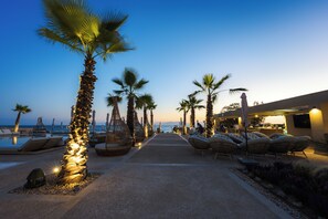 A resort pool area with lounge chairs and palm trees, leading to a bar area with outdoor seating. - Medite Kassandra Resort (Nea Propontida)