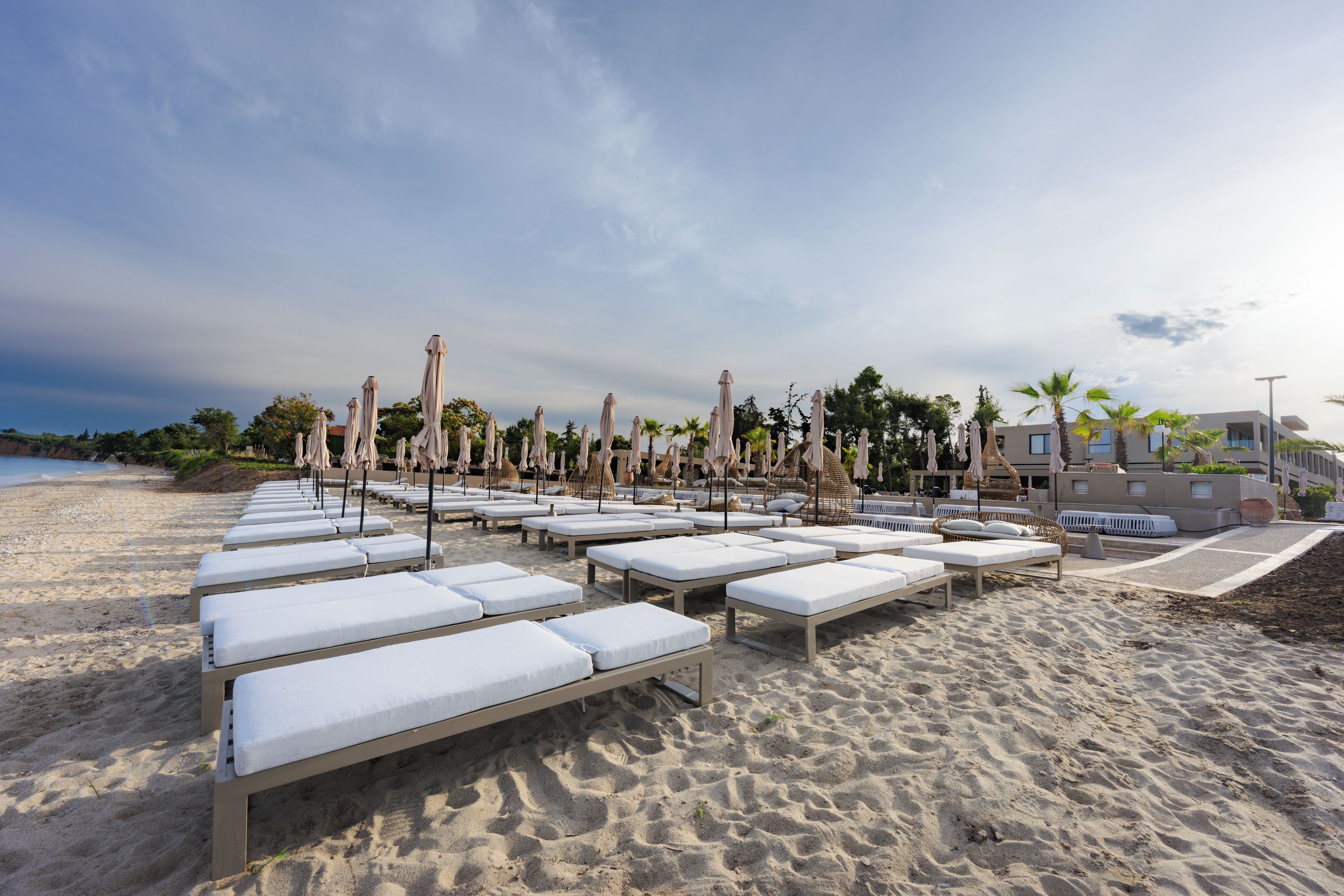 A beachside lounge area with sunbeds and umbrellas, a clear sky, and a building in the background.