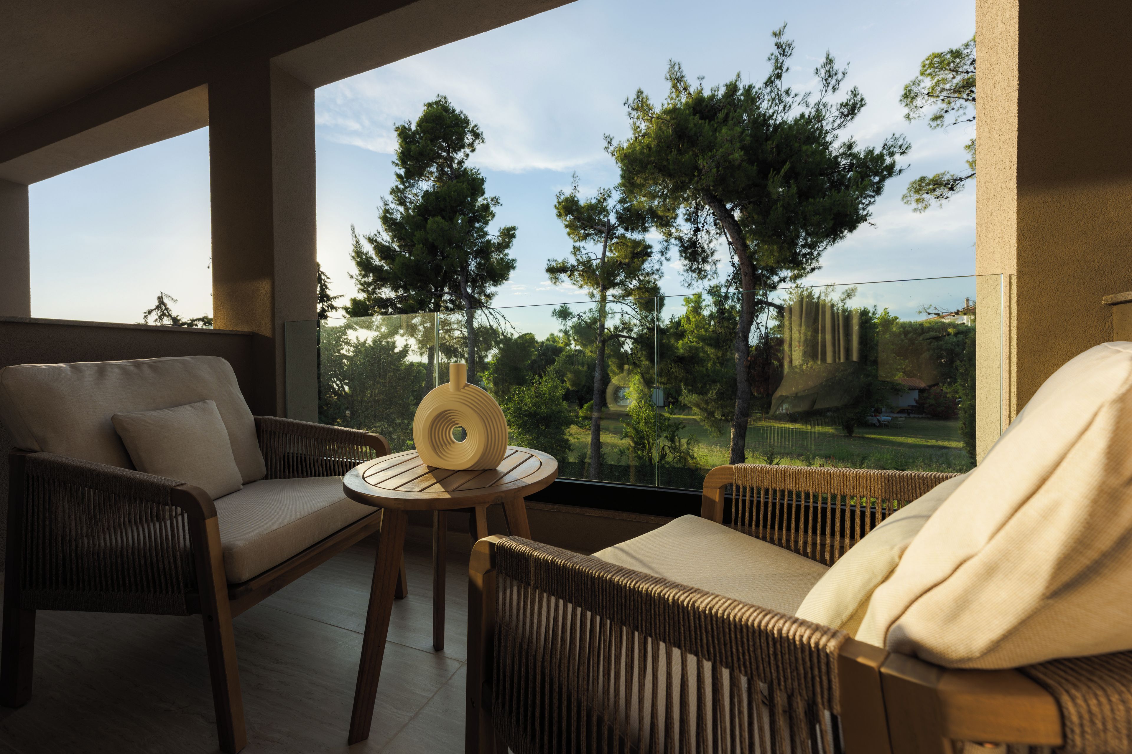 Ein Balkon mit Korbmöbeln, einem runden Tisch und Blick auf Bäume und eine entfernte Landschaft.