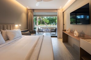 Habitación de hotel con una cama grande, un escritorio, un televisor y vistas a un jardín.