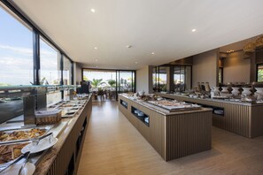 A modern buffet setup with multiple serving stations, a central island, and a view of the outdoors. - Medite Kassandra Resort (Nea Propontida)